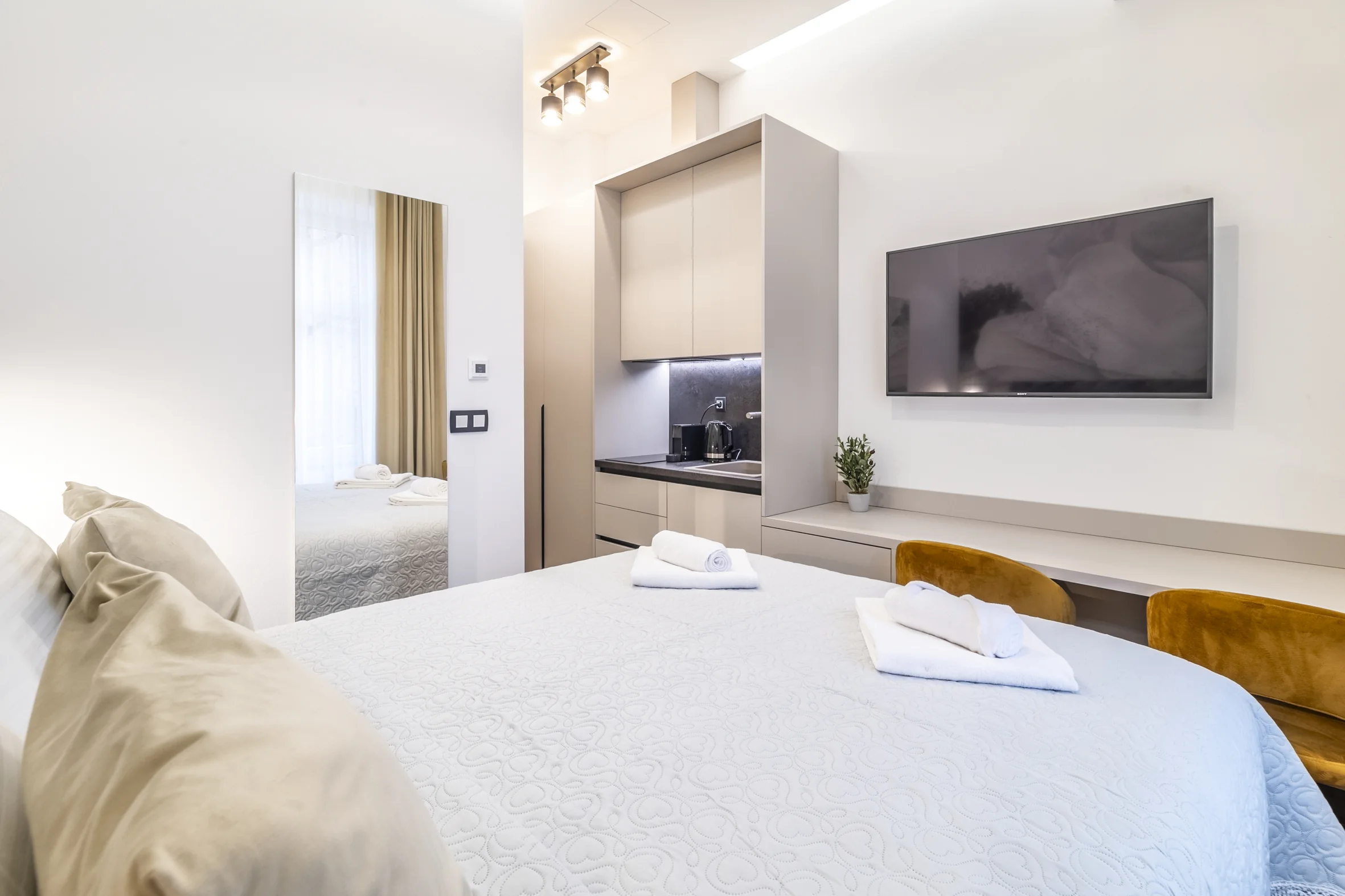 Studio apartment: queen bed, wall-mounted TV, kitchen and gold armchairs